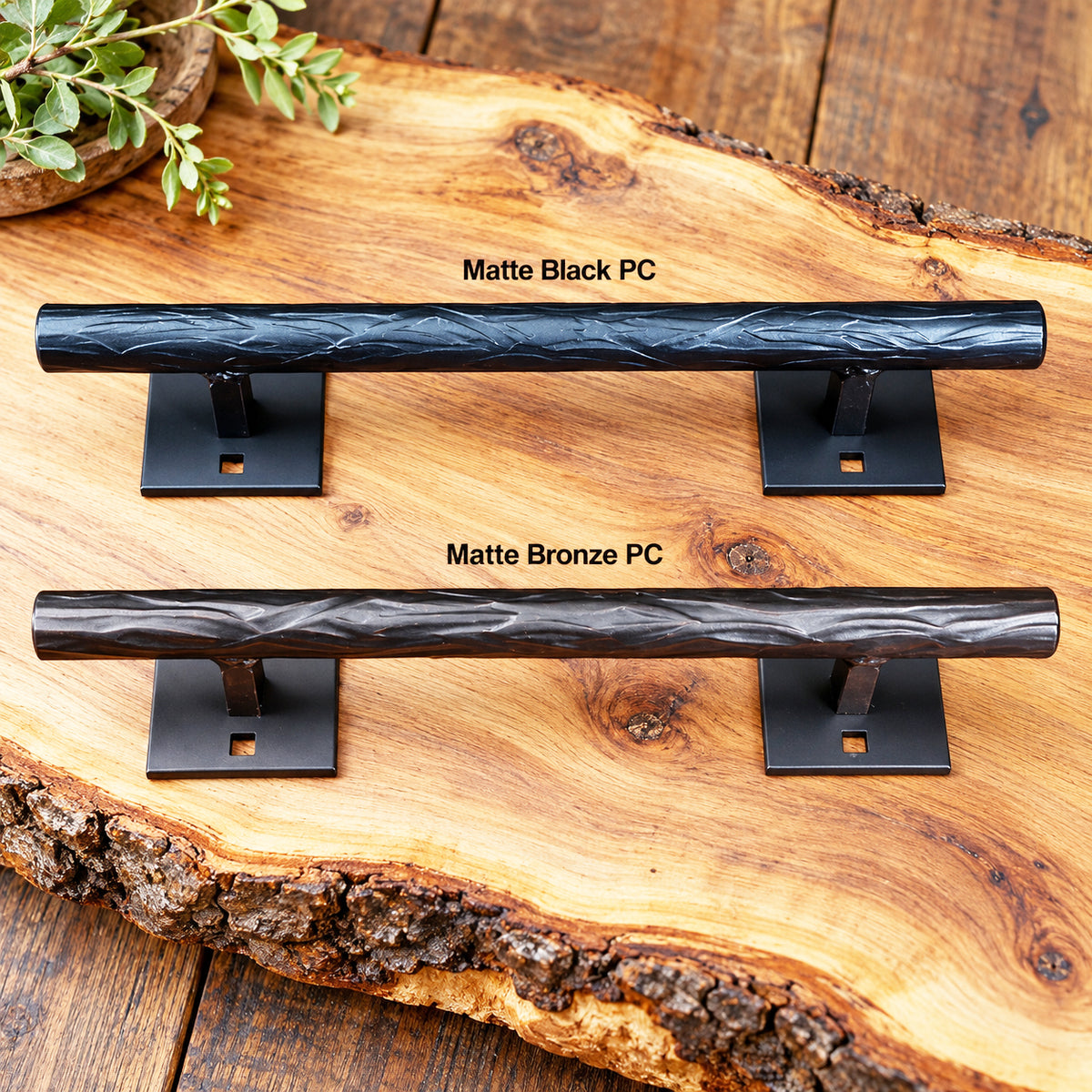 Two horizontal door handles displayed on a rustic wood slab background, labeled 'Matte Black PC' and 'Matte Bronze PC.' The handles are mounted on square wall brackets, and a small plant sprig appears in the top-left corner.