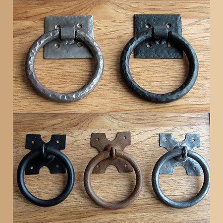 A photo of 5 ring pull handles in black, brass, and silver finishes. 2 ring pull handles feature a hammered texture.