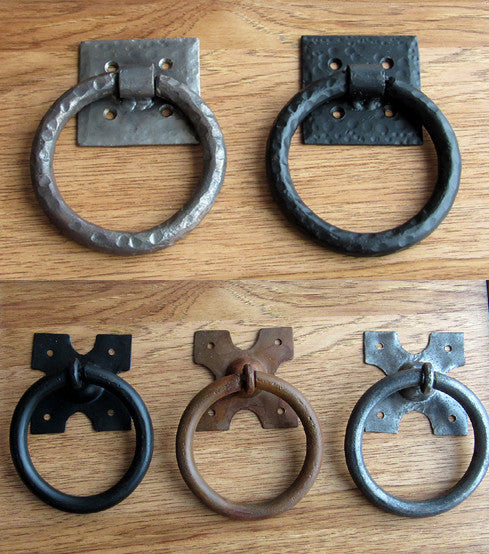 A photo of 5 ring pull handles in black, brass, and silver finishes. 2 ring pull handles feature a hammered texture.