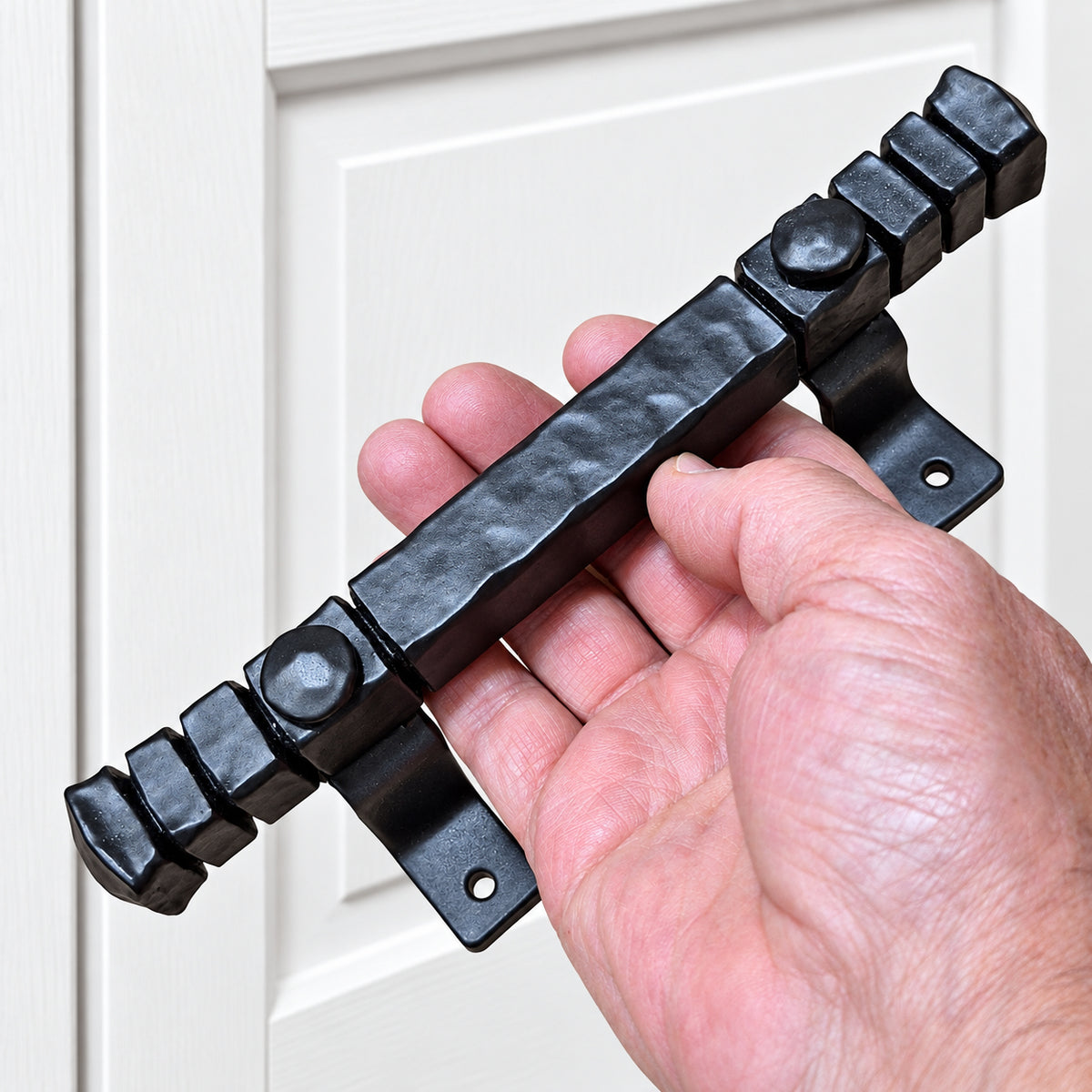 A hand holding a rustic hammered door pull in matte black finish