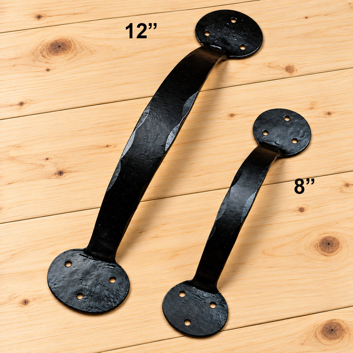 Two black metal cabinet pulls with circular mounting plates, shown on a light wood plank background. One larger pull is labeled 12 inches and one smaller pull is labeled 8 inches.