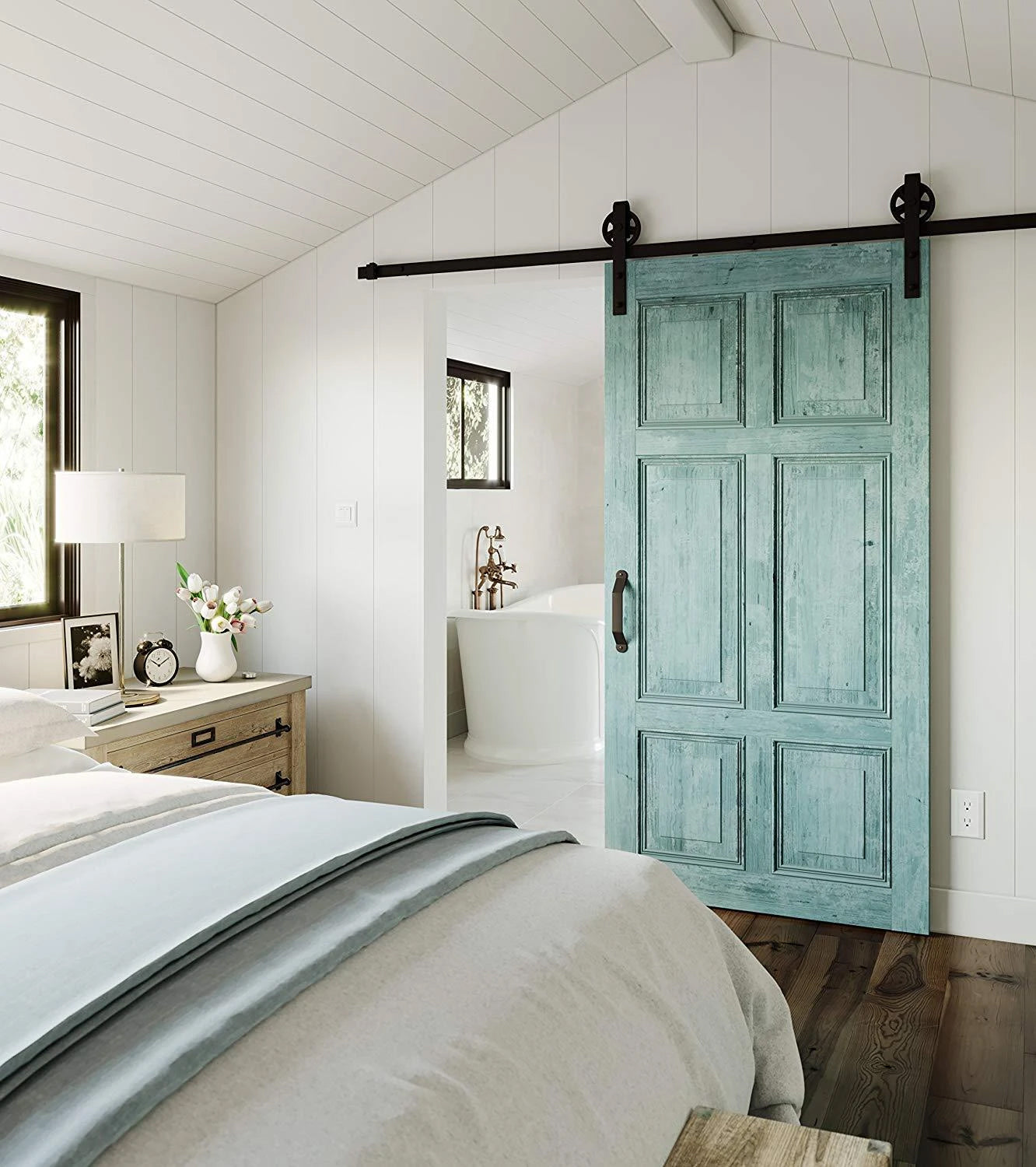 The interior of a bedroom with a white bed, cabinet, sliding barn door, and bathtub in view.